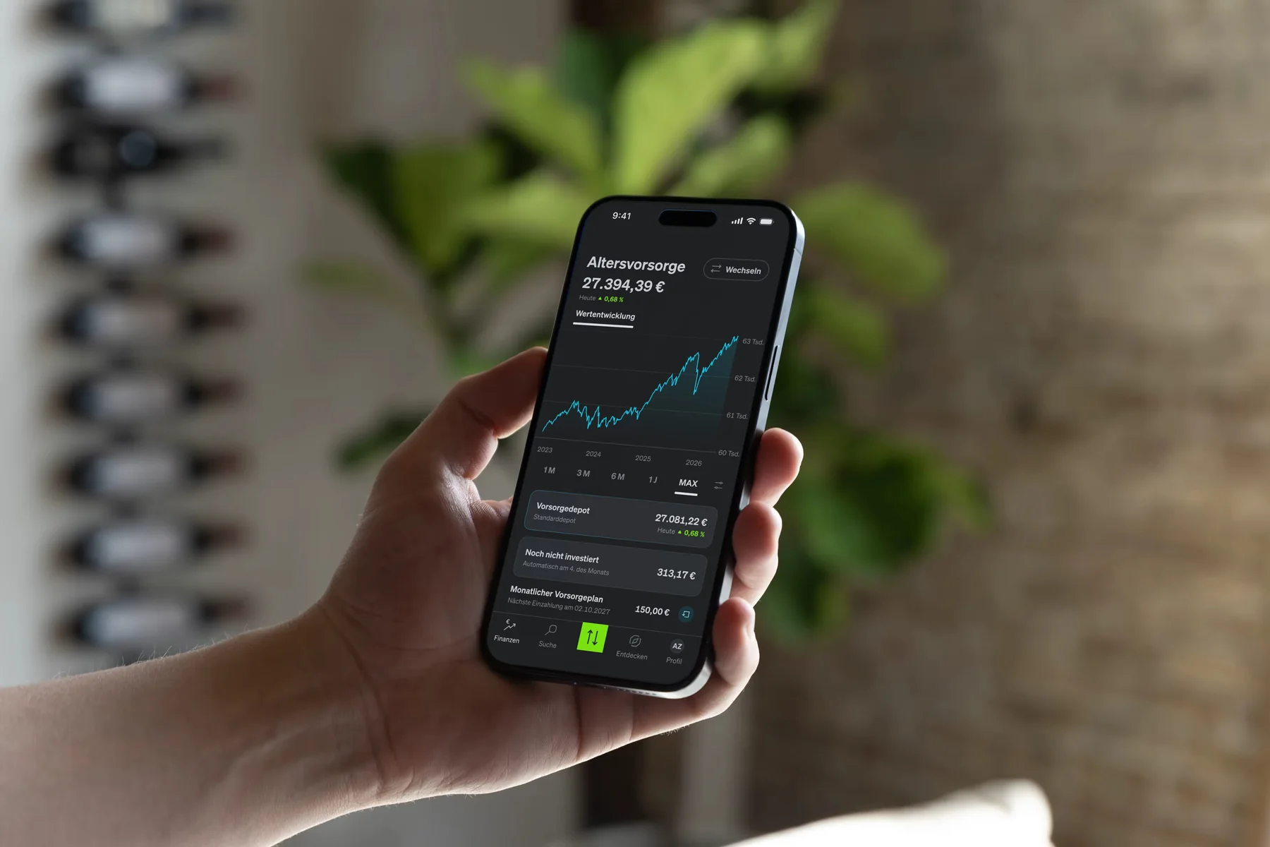 Hand holding an iPhone showing the SMARTBROKER+ retirement portfolio, with plants in the background